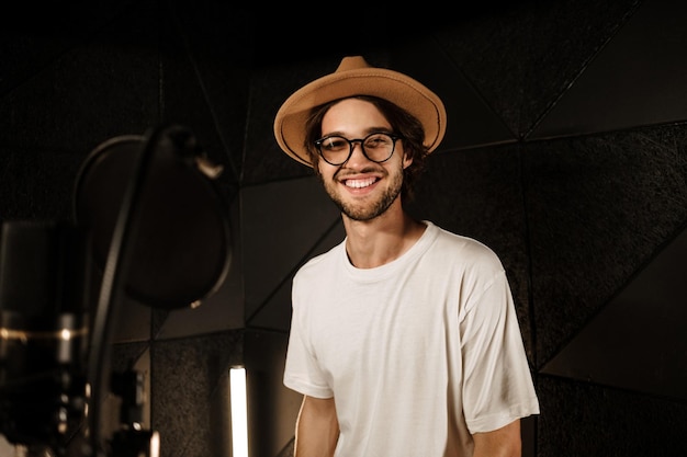 Guapo y elegante cantante masculino mirando felizmente en la cámara grabando una canción para un nuevo álbum en el estudio de sonido