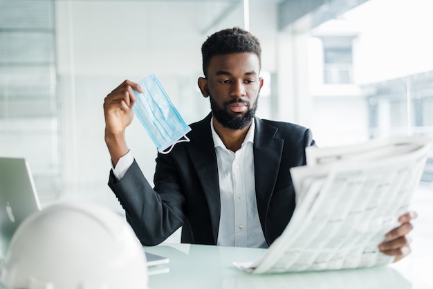 Foto gratuita guapo empresario africano usar máscara médica con periódico en la mañana cerca de la oficina del centro de negocios