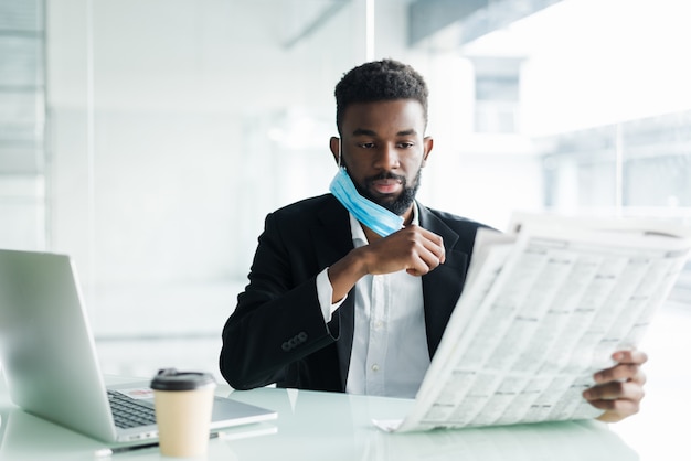 Guapo empresario africano usar máscara médica con periódico en la mañana cerca de la oficina del centro de negocios