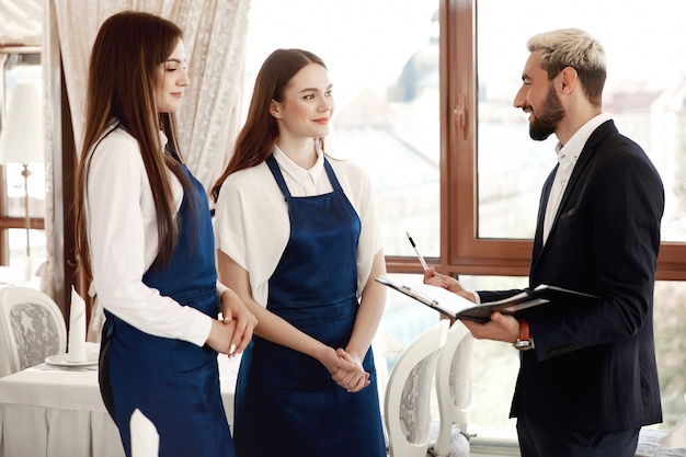 El guapo gerente del restaurante está hablando con las camareras sobre el proceso de trabajo