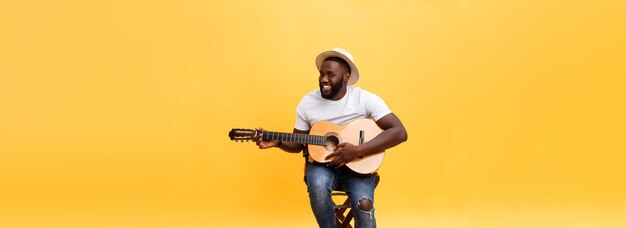 Guapo guitarrista de estilo retro afroamericano tocando guitarra acústica aislado en backgrou amarillo