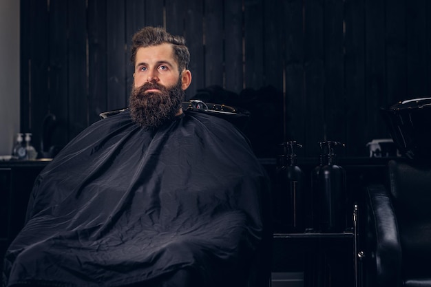 Guapo hombre barbudo con antes de lavar el cabello en un salón de peluquería.