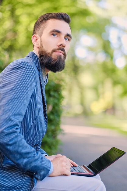 Guapo hombre barbudo usando laptop en un parque.