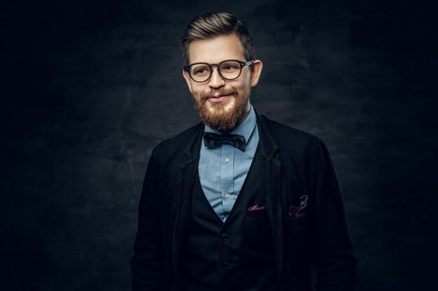 Guapo hombre elegante barbudo en anteojos vestido con un traje azul oscuro con corbata de moño sobre fondo de viñeta gris.