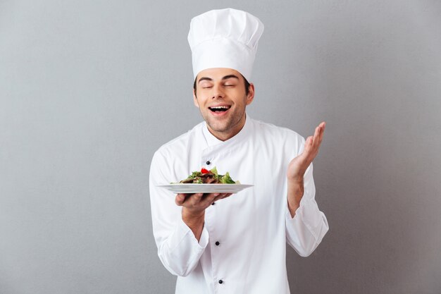 Guapo joven cocinero en ensalada de olor uniforme