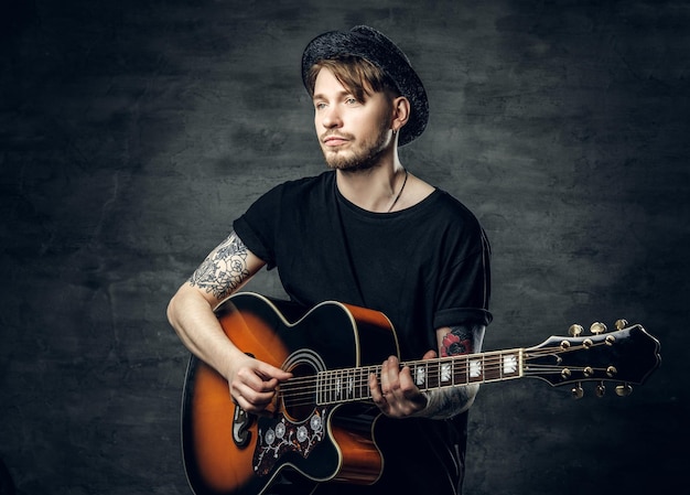 Guapo joven jugador de blues de guitarra acústica con tatuajes en los brazos realizando sus habilidades musicales.