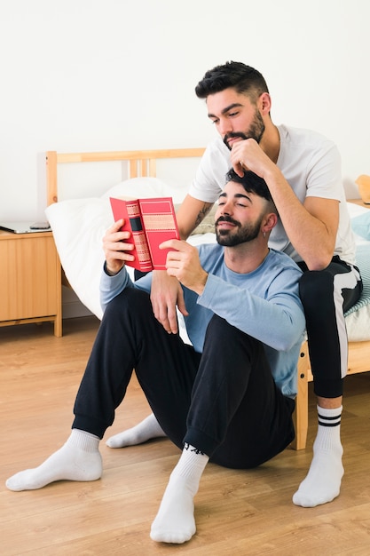 Guapo joven pareja gay juntos leyendo el libro en el dormitorio