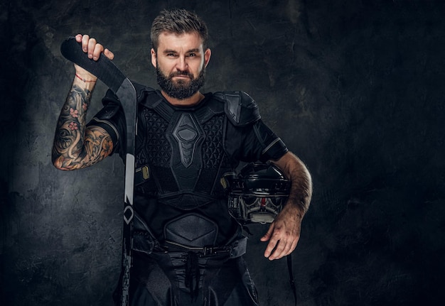 Guapo jugador de hockey tatuado en uniforme está posando para el fotógrafo.