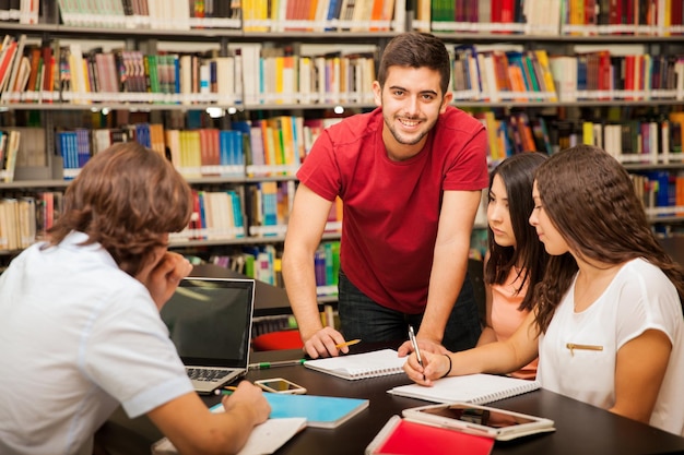 Guapo latino ayudando a sus colegas explicando algo de su trabajo en la biblioteca