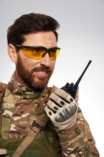 Guapo militar con gafas tácticas amarillas hablando por walkietalkie retrato de soldado sonriente