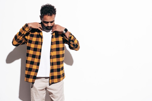 Guapo modelo hipster sonriente Hombre sexy sin afeitar vestido con camisa amarilla de verano y ropa de jeans Hombre de moda posando junto a la pared blanca en el estudio en un día soleado Aislado