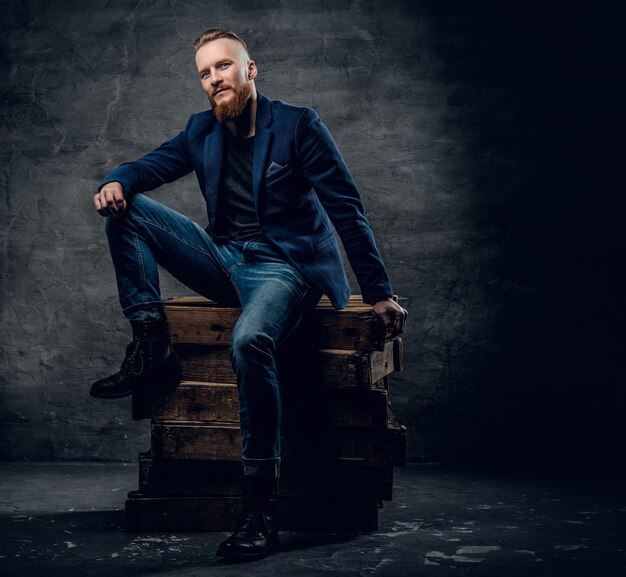 Un guapo pelirrojo vestido con jeans y una camisa posando en una caja de madera.