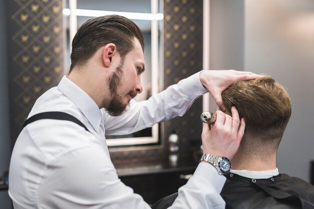 Guapo peluquero que afeita el cabello del cliente