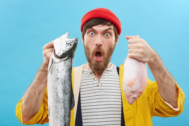 Guapo pescador joven barbudo sosteniendo dos peces que acaba de atrapar