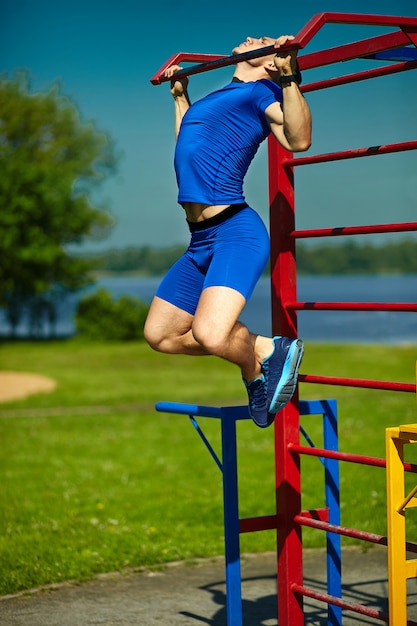 Guapo sano feliz atleta srtong hombre masculino haciendo ejercicio en el parque de la ciudad - conceptos de fitness en un hermoso día de verano en la barra horizontal