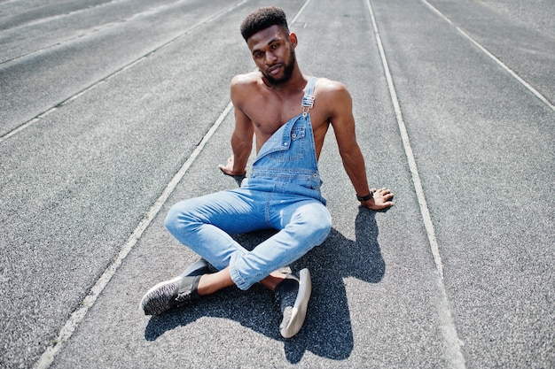 Foto gratuita guapo sexy afroamericano torso desnudo hombre en overoles de jeans sentado en el hipódromo del estadio retrato de hombre negro de moda