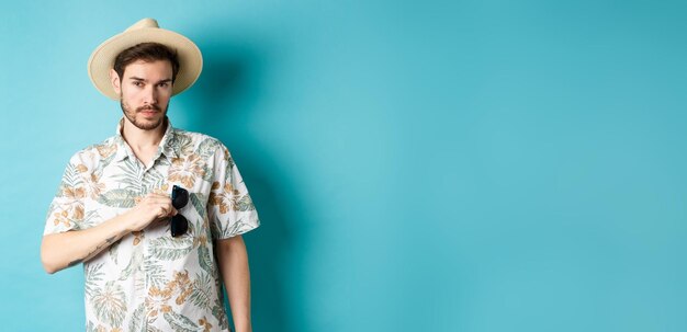 Foto gratuita guapo turista en camisa hawaiana y sombrero de verano puso gafas de sol en el bolsillo yendo de vacaciones suplente