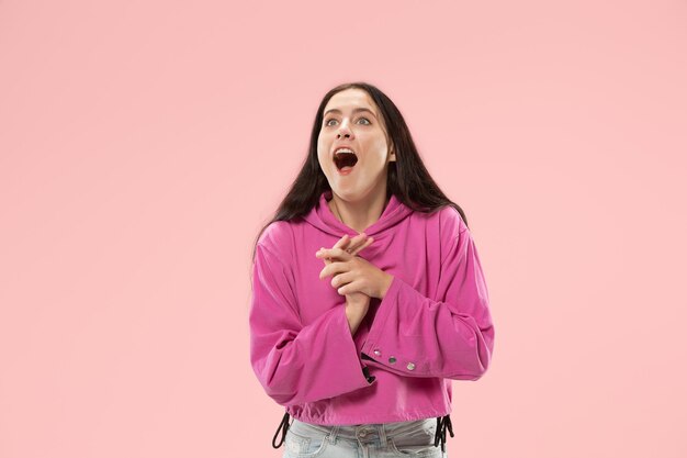 Guau. Hermoso retrato frontal de medio cuerpo femenino aislado sobre fondo de color rosa de estudio. Joven mujer sorprendida emocional de pie con la boca abierta. Las emociones humanas, el concepto de expresión facial. Colores de moda