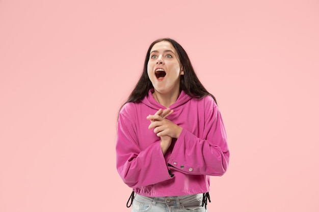 Guau. Hermoso retrato frontal de medio cuerpo femenino aislado sobre fondo de color rosa de estudio. Joven mujer sorprendida emocional de pie con la boca abierta. Las emociones humanas, el concepto de expresión facial. Colores de moda