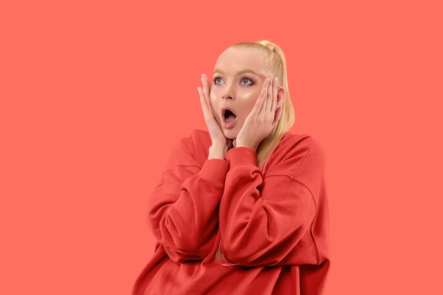 Guau. Hermoso retrato frontal de medio cuerpo femenino aislado sobre fondo de estudio de coral. Joven mujer emocional sorprendida de pie con la boca abierta. Las emociones humanas, el concepto de expresión facial. Colores de moda