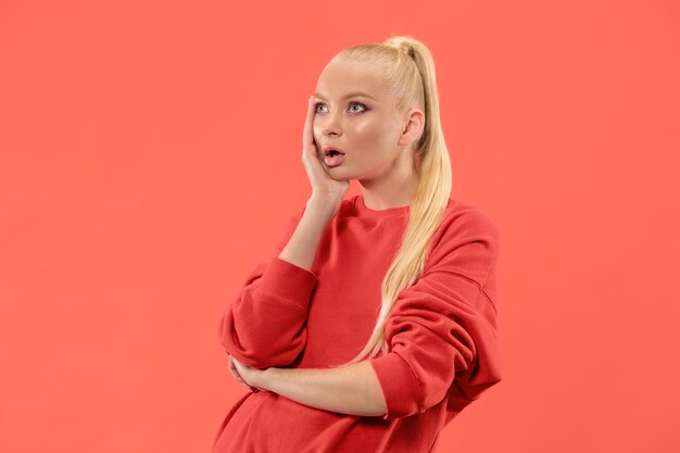 Guau. Hermoso retrato frontal de medio cuerpo femenino aislado sobre fondo de estudio de coral. Joven mujer emocional sorprendida de pie con la boca abierta. Las emociones humanas, el concepto de expresión facial. Colores de moda