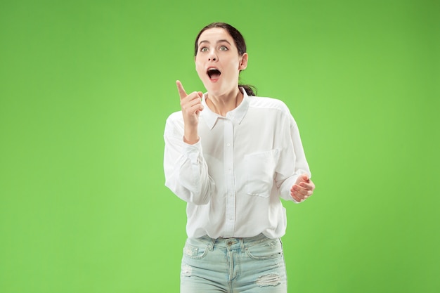 Guau. Hermoso retrato frontal de medio cuerpo femenino aislado sobre fondo verde. Joven mujer sorprendida emocional de pie con la boca abierta