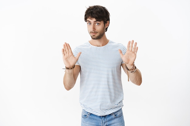 Foto gratuita guau, más lento. retrato de joven confuso e intenso desencadenado guapo macho mostrando gesto de parada pidiendo sujetar caballos como novia fue demasiado lejos pidiendo estar fresco y calmado sobre la pared gris