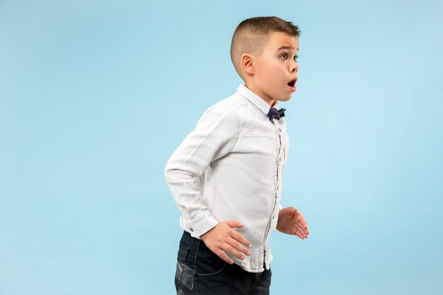 Guau. Retrato frontal de medio cuerpo masculino atractivo sobre fondo de color azul de estudio. Joven muchacho adolescente sorprendido emocional de pie con la boca abierta. Las emociones humanas, el concepto de expresión facial. Colores de moda