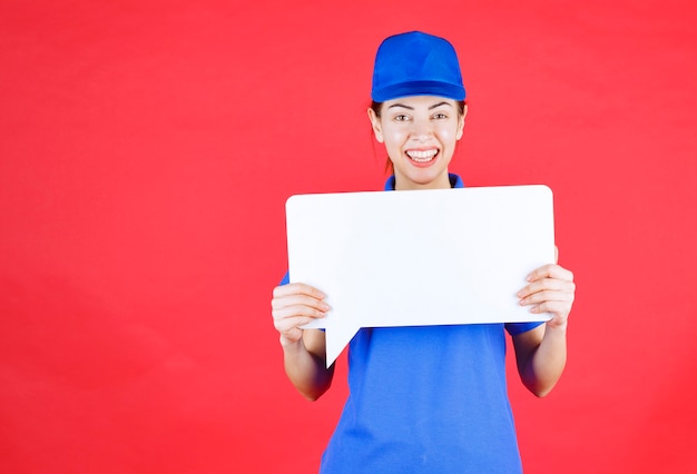 Guía femenina en uniforme azul sosteniendo un tablero de información rectangular blanco.