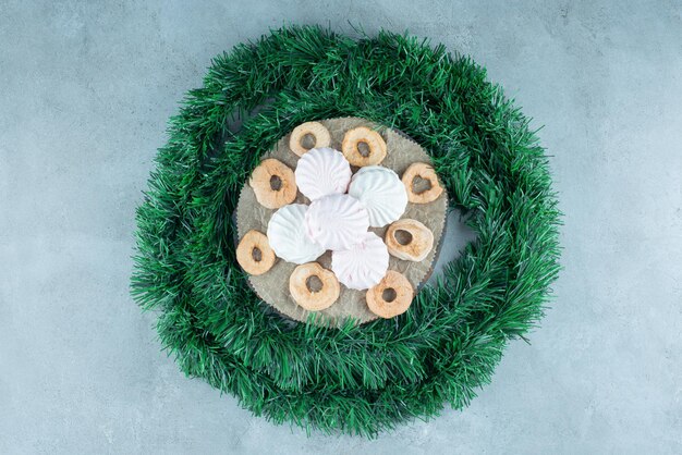 Guirnalda envuelta alrededor de una tabla con galletas y rodajas de manzana secas sobre mármol.