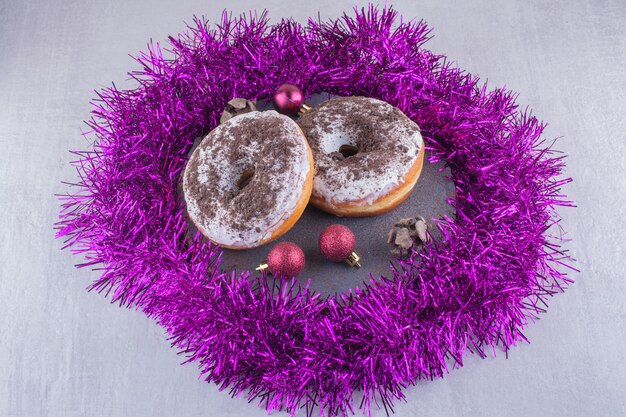 Guirnalda púrpura alrededor de donas glaseadas sobre una tabla de madera sobre fondo blanco.