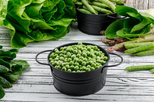 Foto gratuita guisantes en una cacerola con espárragos, acedera, bok choy, lechuga, vainas verdes vista de ángulo alto en una pared de madera