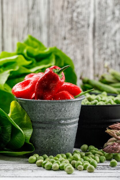 Guisantes y pimientos con lechuga, vainas verdes, espárragos, bok choy en cubos en la pared de madera sucia, vista lateral.