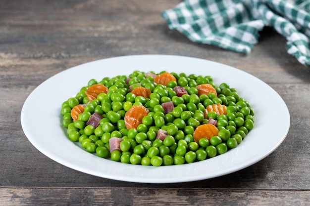 Guisantes verdes con jamón serrano y zanahoria sobre mesa de madera