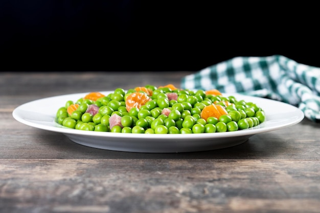 Guisantes verdes con jamón serrano y zanahoria sobre mesa de madera