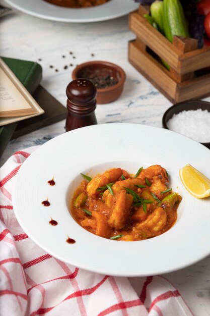 Guiso de patas de pollo en salsa de tomate en un tazón blanco con verduras y limón.