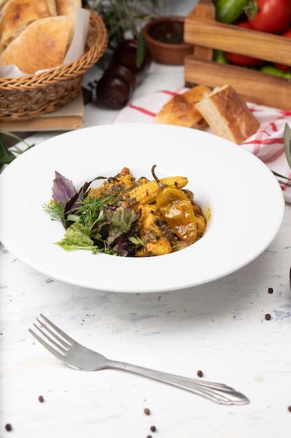 Guiso de verduras con carne, trozos de maíz, ají y vegetales, basílicos, perejil en plato blanco.