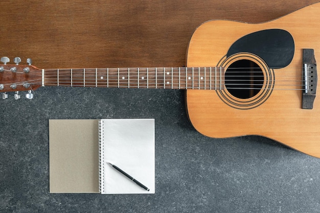 Foto gratuita guitarra acústica y cuaderno de notas sobre un fondo de madera y negro con textura