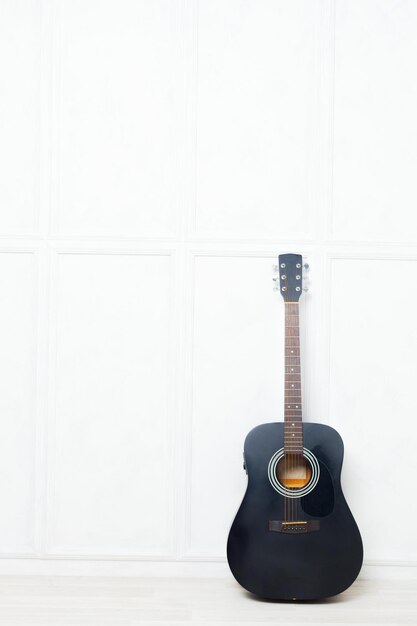 Guitarra apoyada frente a una pared blanca