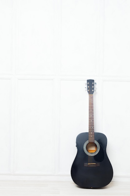 Guitarra apoyada frente a una pared blanca