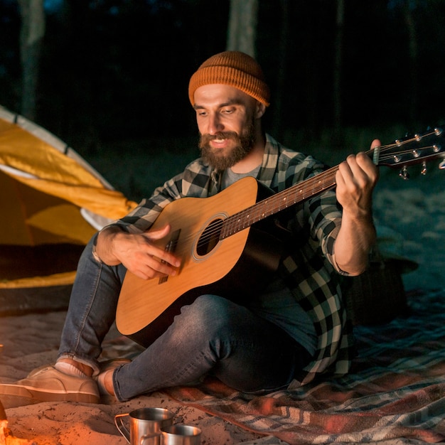 Guitarrista acampando y cantando junto a una hoguera.