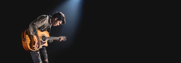 Foto gratuita un guitarrista masculino toca una guitarra acústica en un fondo oscuro del escenario