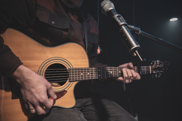 El guitarrista toca una guitarra acústica con una cejilla frente a un micrófono
