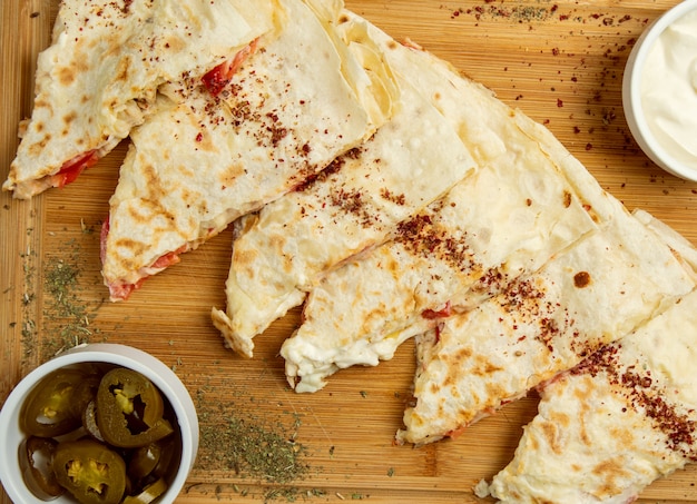 Gutab de carne tradicional, qutab, gozleme sobre tabla de madera con sumakh, turshu y yogurt.