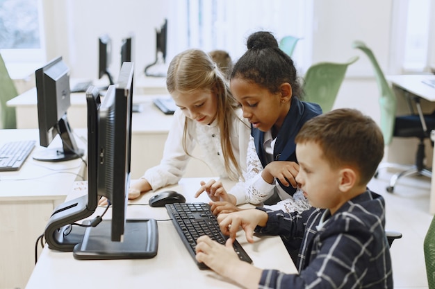 Guy y la niña están sentados a la mesa. Niña africana en la clase de informática. Niños jugando juegos de computadora.