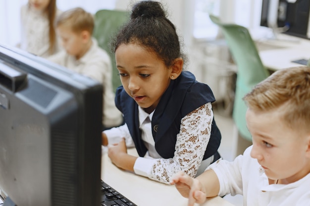 Guy y la niña están sentados a la mesa. Niña africana en la clase de informática. Niños jugando juegos de computadora.