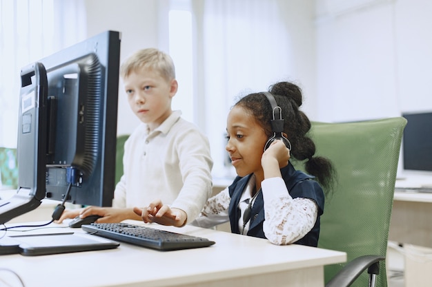 Guy y la niña están sentados a la mesa. Niña africana en la clase de informática. Niños jugando juegos de computadora.