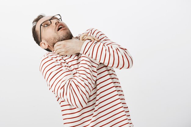 Guy quiere suicidarse para no escuchar más historias aburridas. Retrato de gracioso hombre europeo con gafas, tomados de la mano en el cuello y doblando hacia atrás