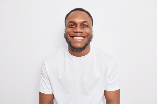 Guy sonríe con dientes parece felizmente feliz de recibir elogios vestido con ropa casual aislado en blanco