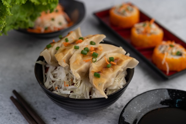 Gyoza en una taza negra con una taza de salsa.